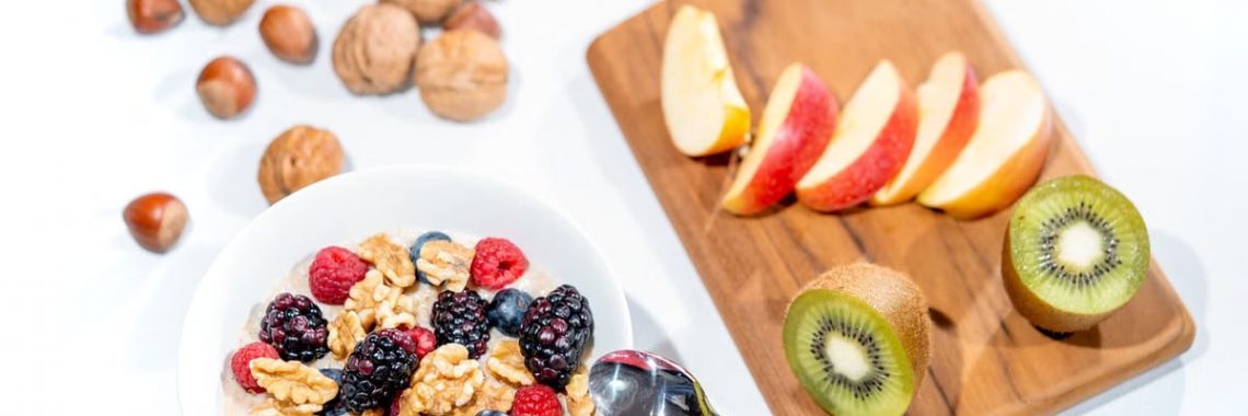 A nutritious breakfast bowl featuring fresh berries and walnuts, served with sliced fruit and kiwi.